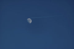 Diego F. Parra - A jet leaves a contrail near a waxing gibbous moon under a bright blue sky, highlighting aviation and astronomy.