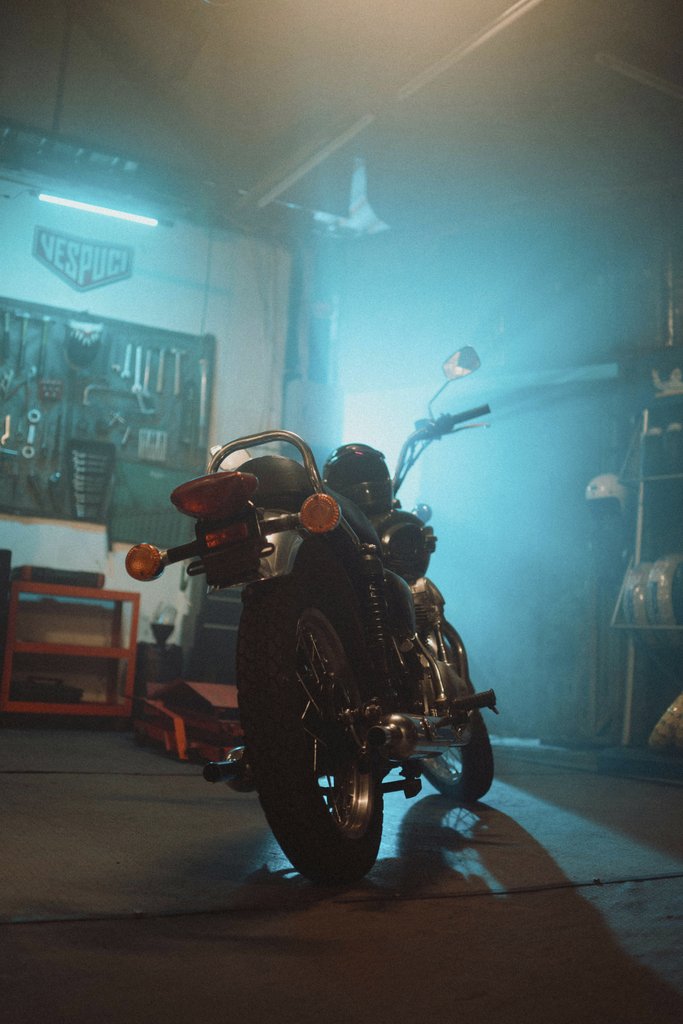 Nandi Gustian - A classic motorcycle parked in a dimly lit garage with blue and orange tones.