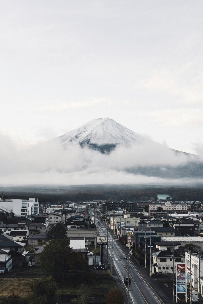 Felipe Alves - A captivating view of Mount Fuji surrounded by clouds, towering over a Japanese town with clear skies.