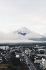 Felipe Alves - A captivating view of Mount Fuji surrounded by clouds, towering over a Japanese town with clear skies.