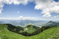 Wolfram K - Stunning view of rolling hills and mountains under a bright blue sky with fluffy clouds.