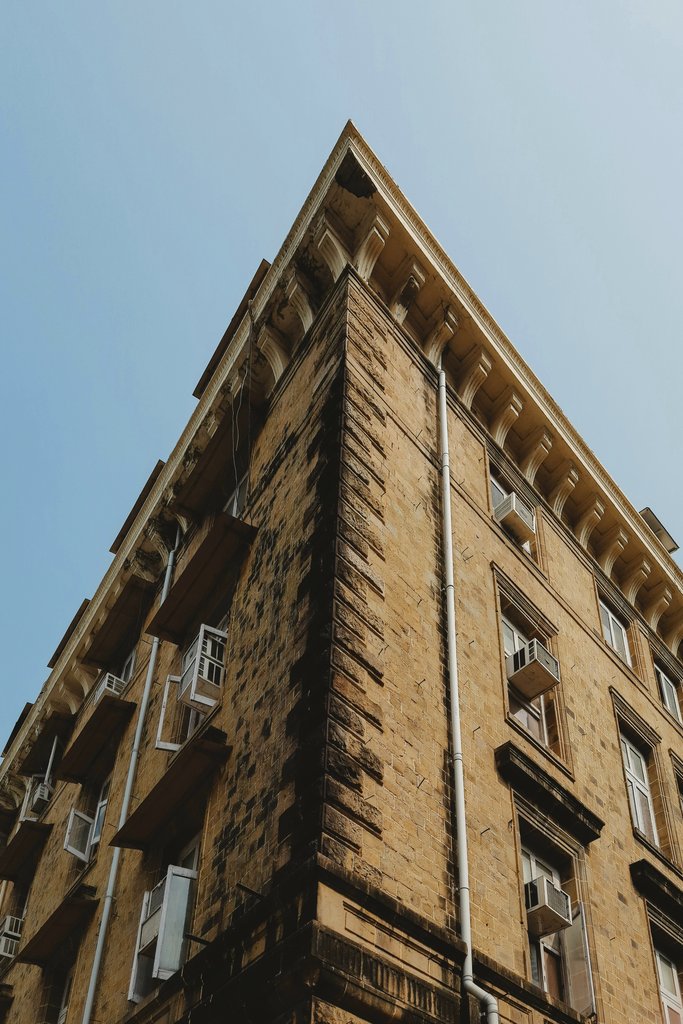 Keith Lobo - Low angle view of a weathered building facade with air conditioners set against a clear blue sky.