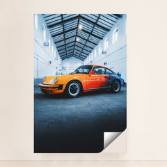This photo features an orange and red classic Porsche sports car parked inside a tall industrial warehouse, unframed.