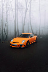 Orange Porsche in the Mist: an orange Porsche 911 GT3 RS in a foggy forest, showcasing its bold design and black wheels.