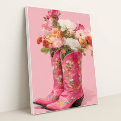 This artwork shows two pink floral cowboy boots filled with colorful roses and flowers against a solid pink background, in a white frame.