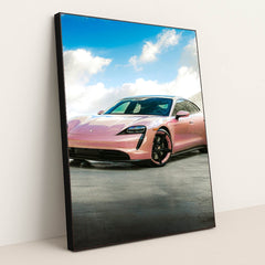 This photo shows a pink Porsche Taycan electric sports car parked outside under a blue sky with clouds, in a black frame.