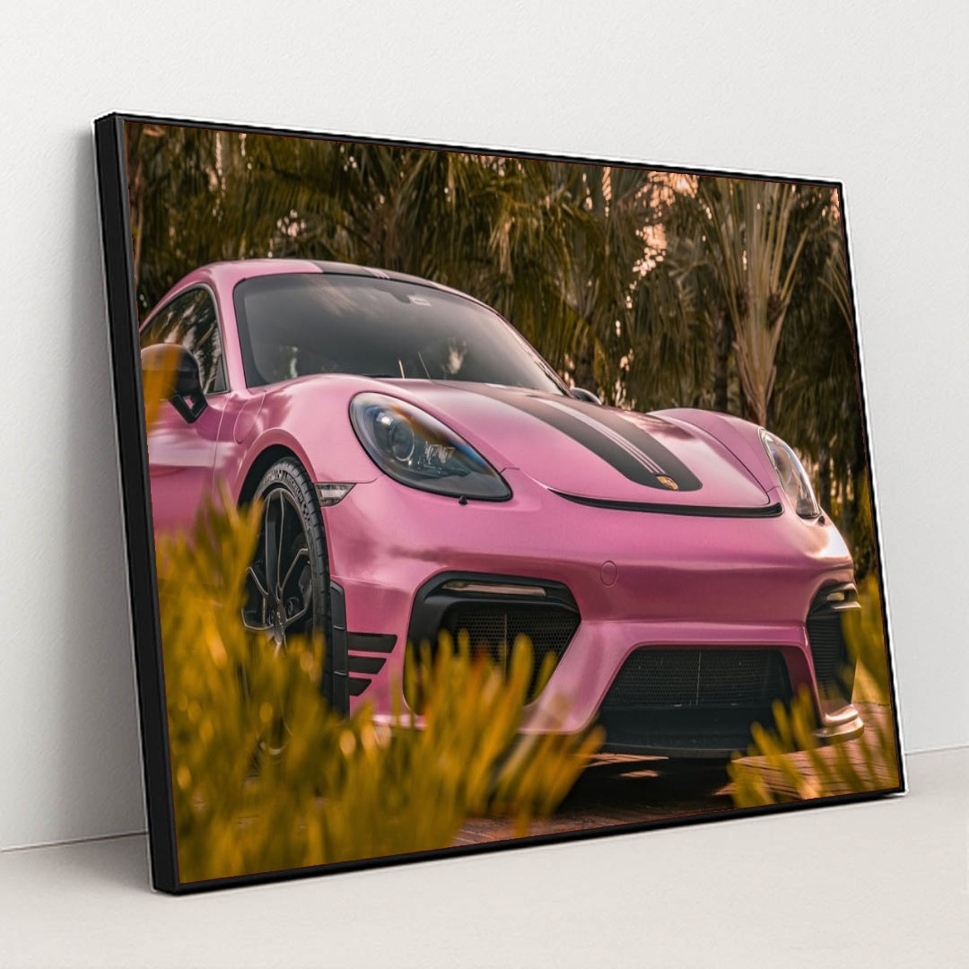 This photo shows a pink Porsche sports car with black stripes parked near tropical palm trees, in a black frame.