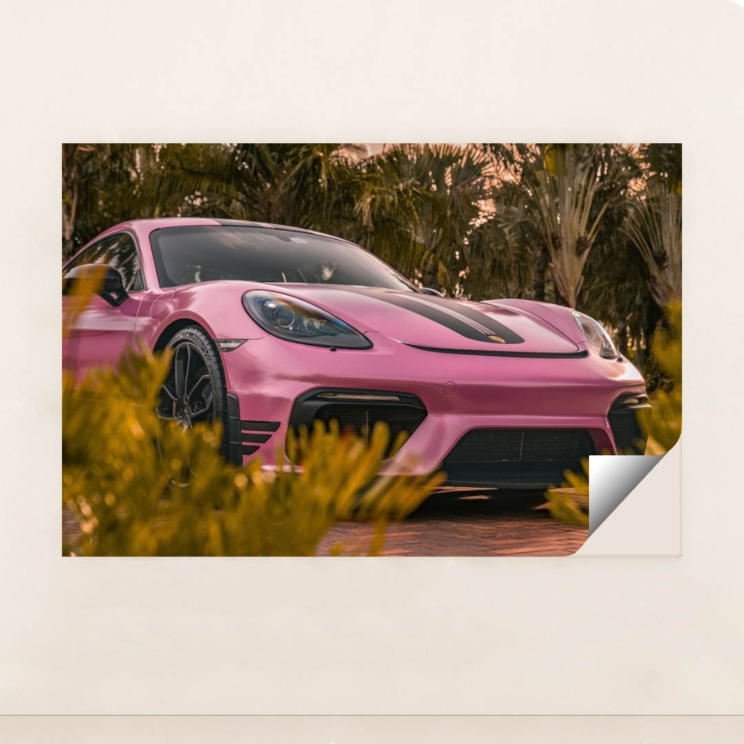This photo shows a pink Porsche sports car with black stripes parked near tropical palm trees, unframed.
