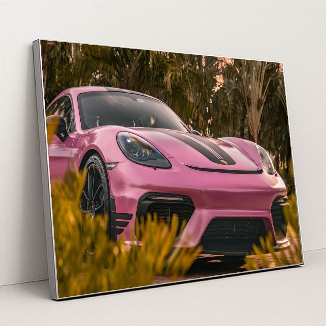 This photo shows a pink Porsche sports car with black stripes parked near tropical palm trees, in a silver frame.