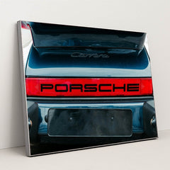This photo shows the rear of a classic Porsche Carrera with a bold red Porsche logo and open trunk, in a silver frame.