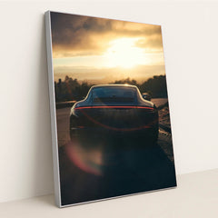 This photo shows the rear view of a Porsche sports car parked on a scenic hill at sunset with lens flare, in a silver frame.