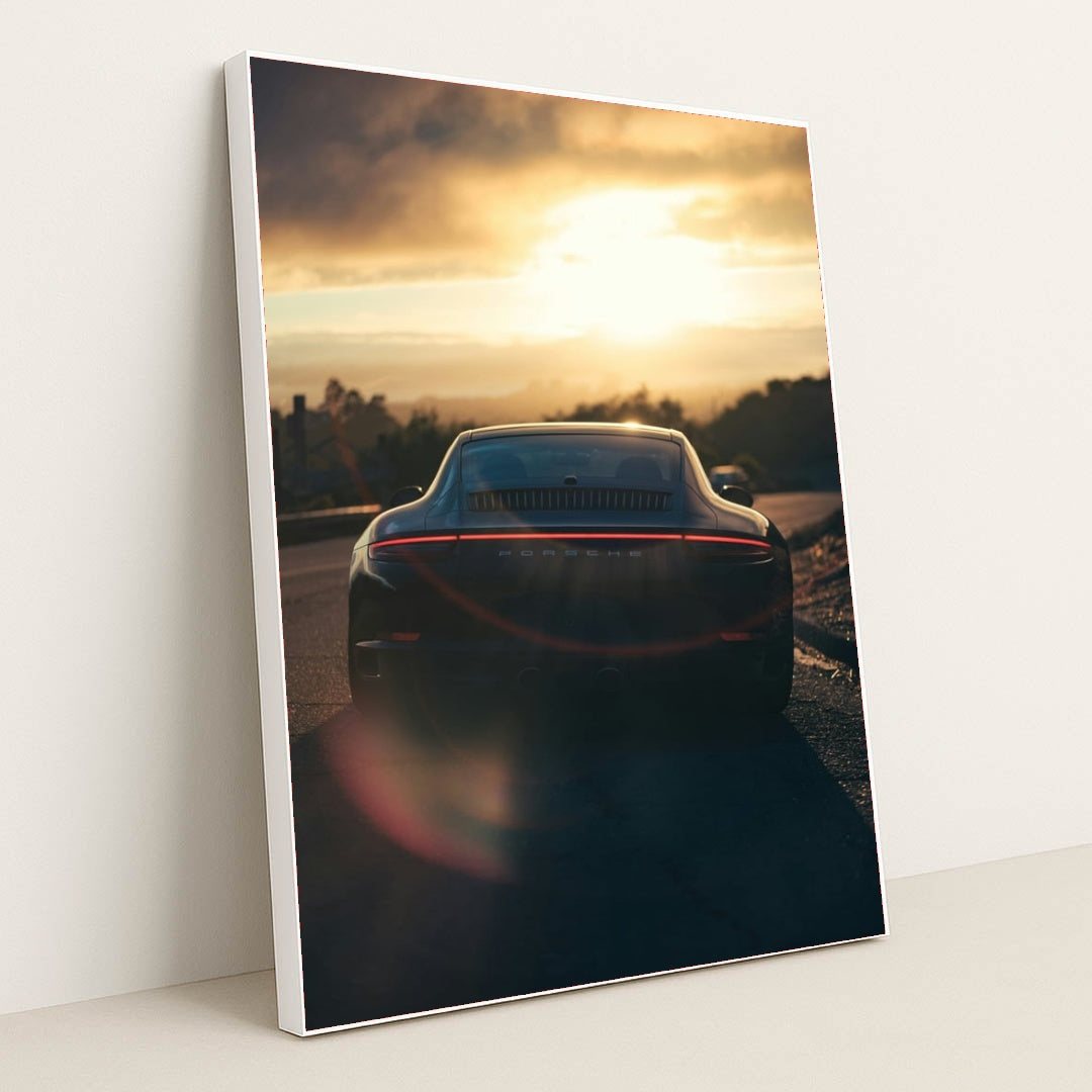 This photo shows the rear view of a Porsche sports car parked on a scenic hill at sunset with lens flare, in a white frame.