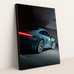 This photo shows a silver Porsche sports car with number 63 and glowing taillights in a modern concrete garage, in a black frame.