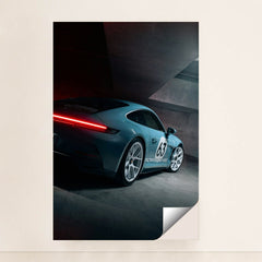 This photo shows a silver Porsche sports car with number 63 and glowing taillights in a modern concrete garage, unframed.