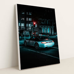 This photo shows a silver Porsche 911 coupe waiting at a red traffic light on a city street at night, in a white frame.