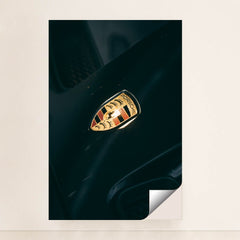 This photo shows a close-up of a classic gold and black Porsche crest badge on a dark car hood, unframed.