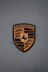 Porsche Crest in the Rain on slate-gray hood with water droplets accentuating the badge's details, ideal for car wall art.