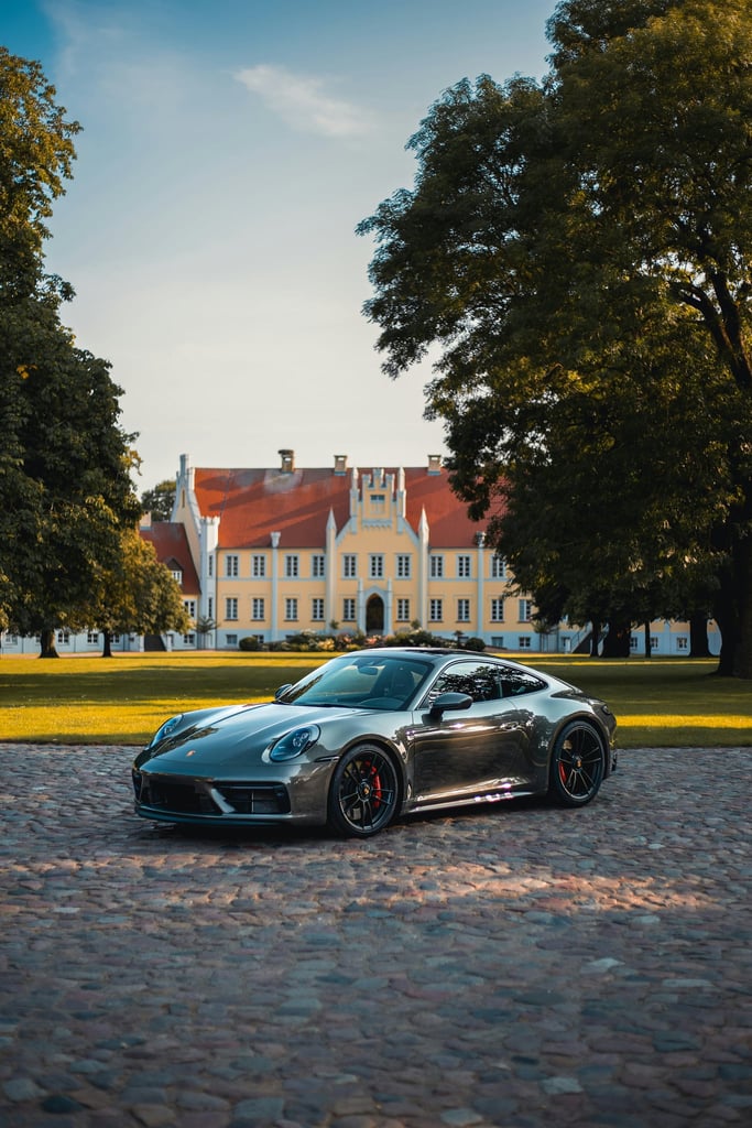 Porsche 911 at the Estate parked on a cobblestone drive, framed by trees and historic architecture, showcasing luxury car wall art.