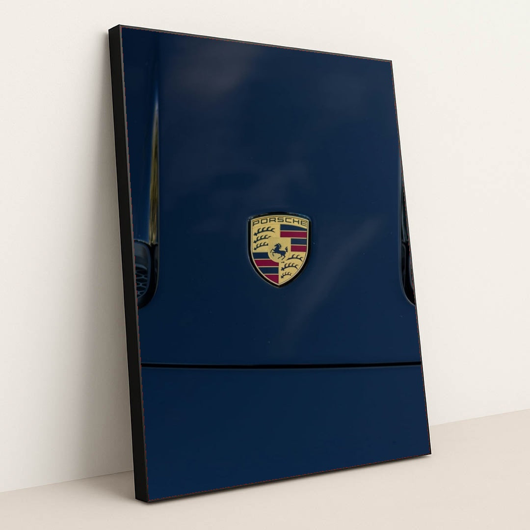 This photo features a Porsche emblem on the hood of a dark blue car, in a black frame.