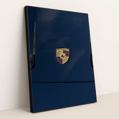 This photo features a Porsche emblem on the hood of a dark blue car, in a black frame.