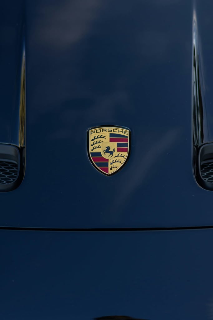 This photo features a Porsche emblem on the hood of a dark blue car.