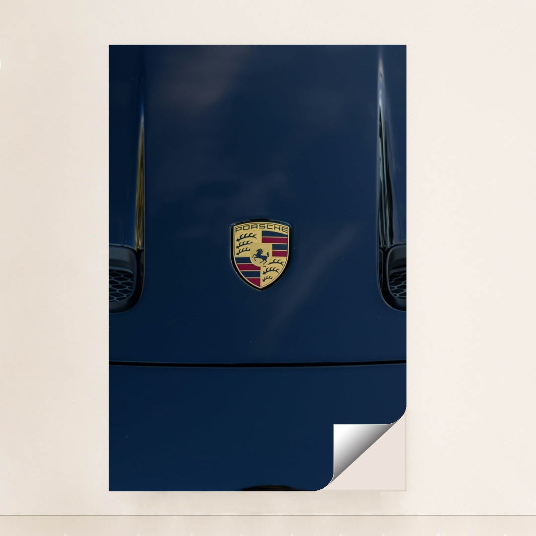 This photo features a Porsche emblem on the hood of a dark blue car, unframed.