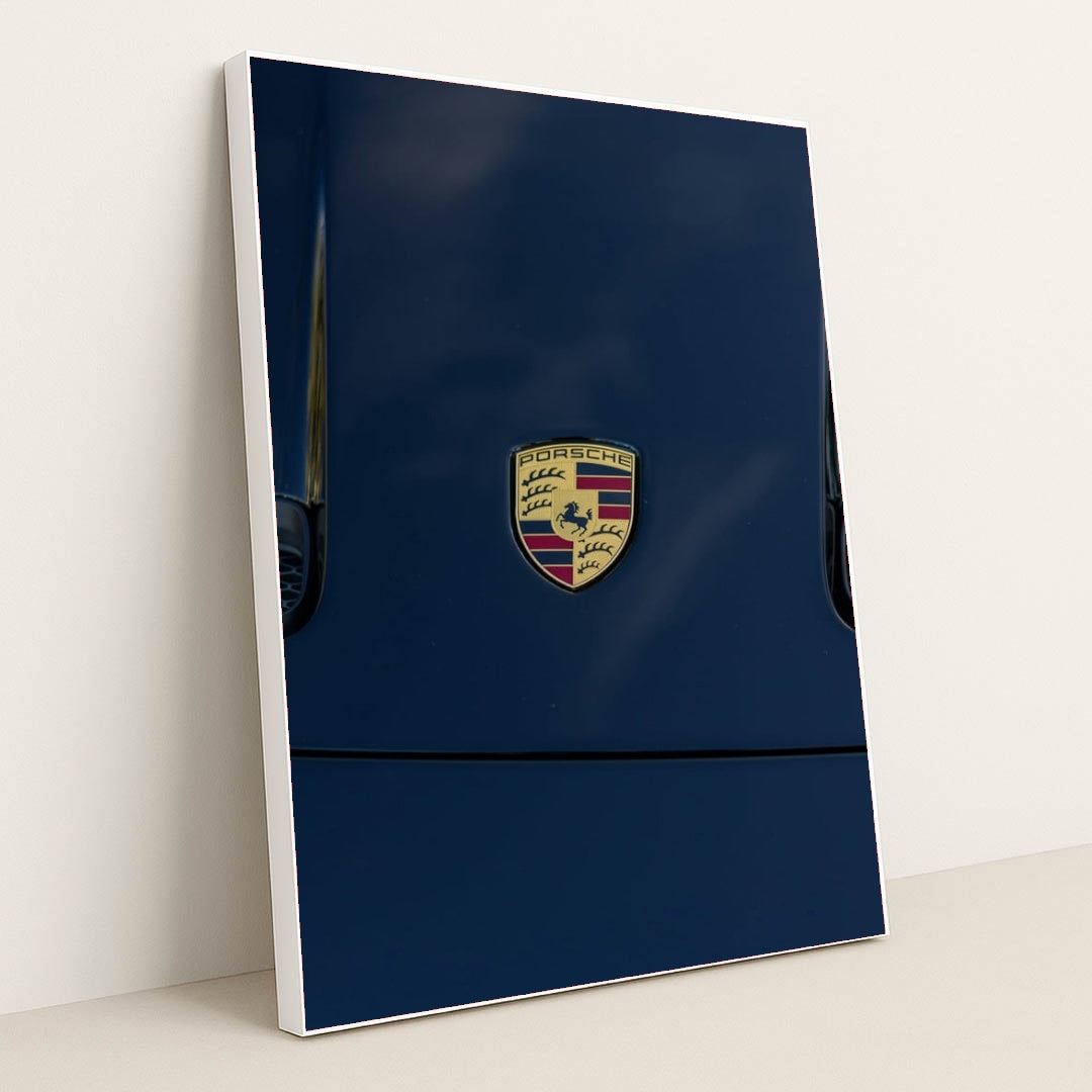 This photo features a Porsche emblem on the hood of a dark blue car, in a white frame.