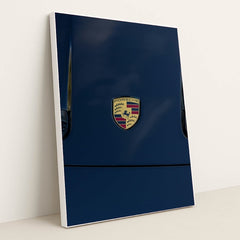 This photo features a Porsche emblem on the hood of a dark blue car, in a white frame.