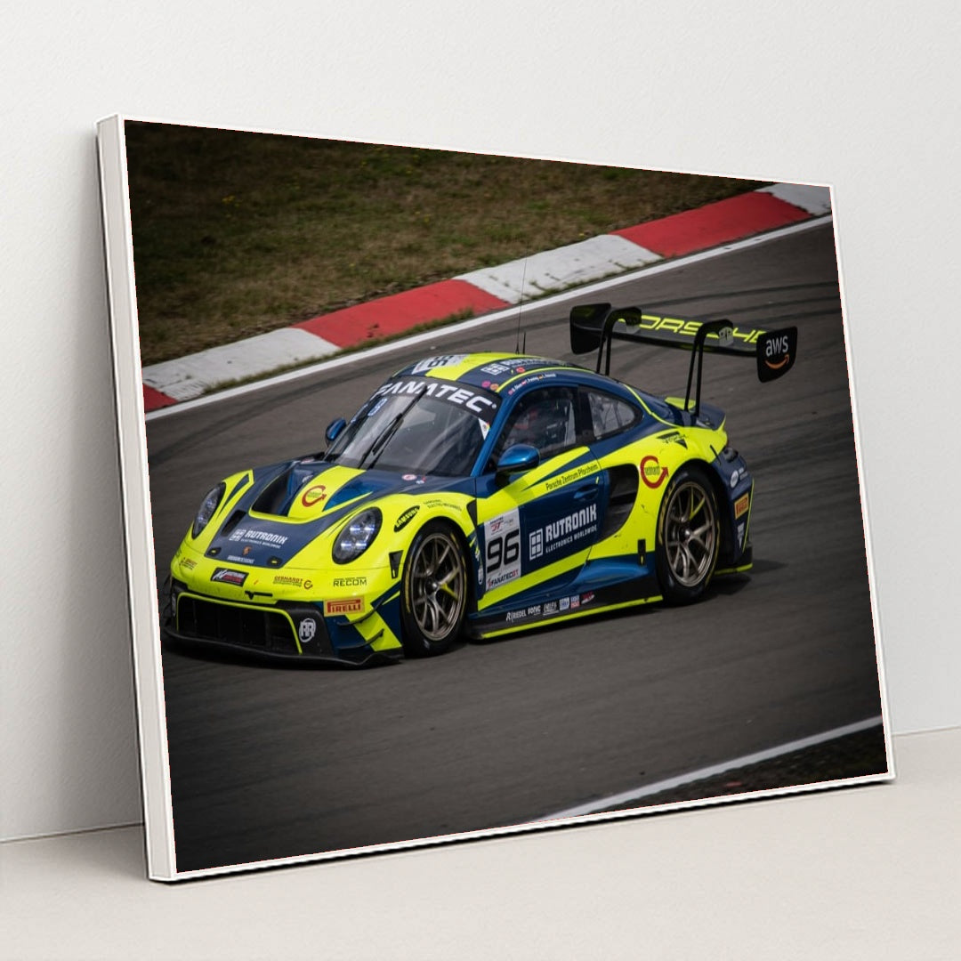 This photo shows a blue and yellow Porsche race car numbered 96 on a racetrack, in a white frame.