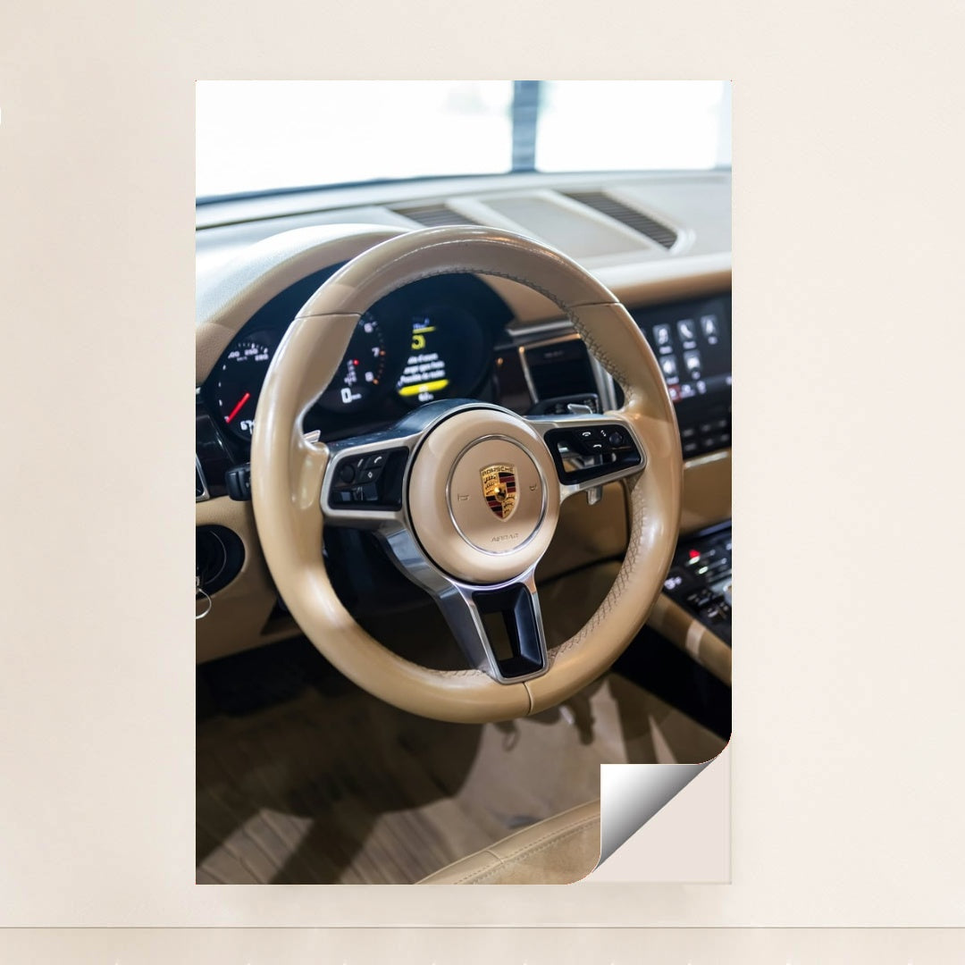 This photo shows the tan leather steering wheel and dashboard of a Porsche with the crest emblem in the center, unframed.