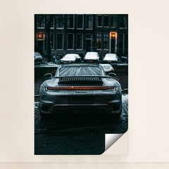 This photo shows the rear view of a silver Porsche sports car covered in raindrops on a city street at night, unframed.