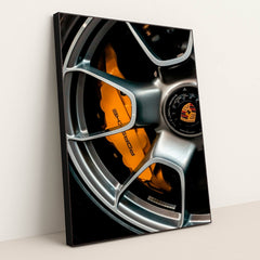 This photo shows a close-up of a silver Porsche wheel with an orange brake caliper and crest logo, in a black frame.