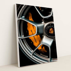 This photo shows a close-up of a silver Porsche wheel with an orange brake caliper and crest logo, in a white frame.