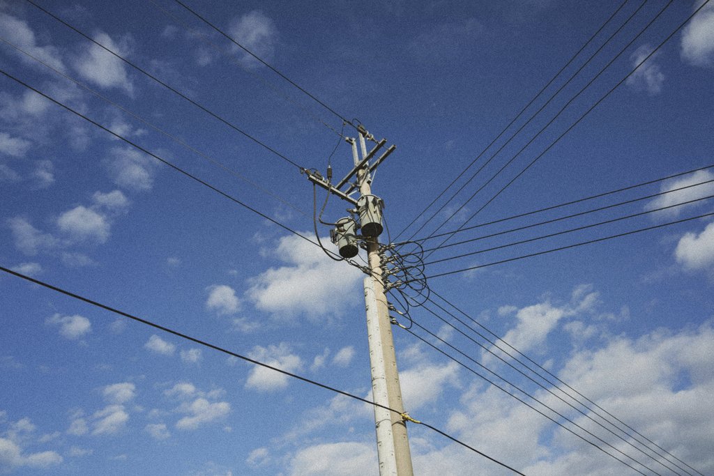 Matthias Schleiden - A utility pole with electrical lines stretching across a bright blue sky with scattered clouds.
