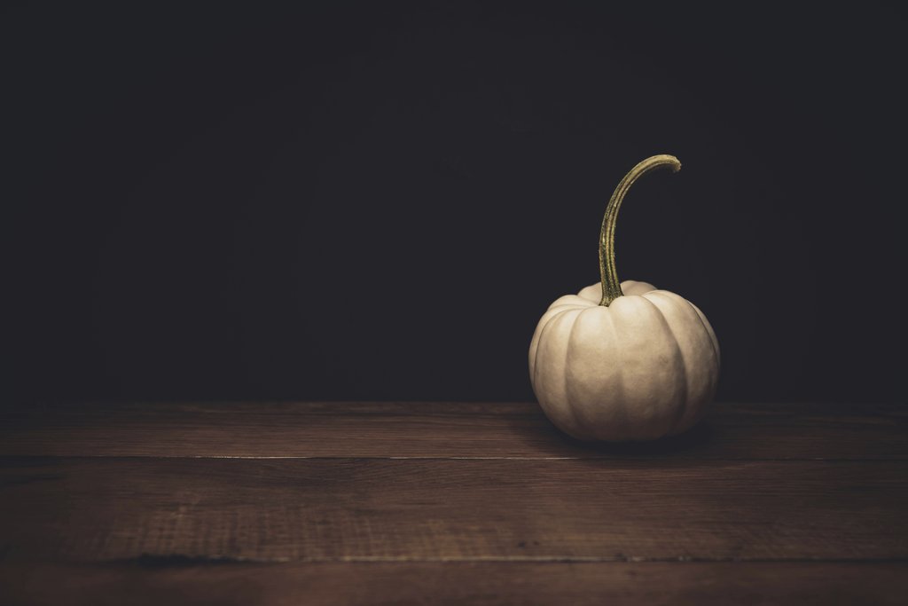 Tim Mossholder - A minimalist still life of a white pumpkin on a wooden surface with dark background.