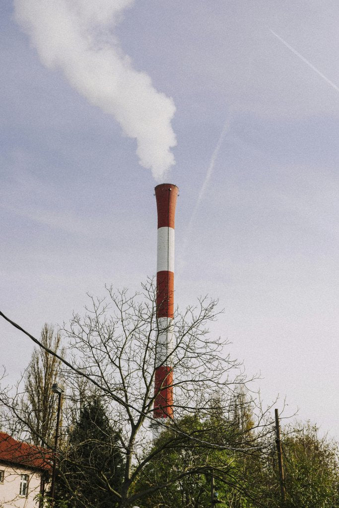 Kelly - A red and white industrial chimney releasing smoke into a clear spring sky.