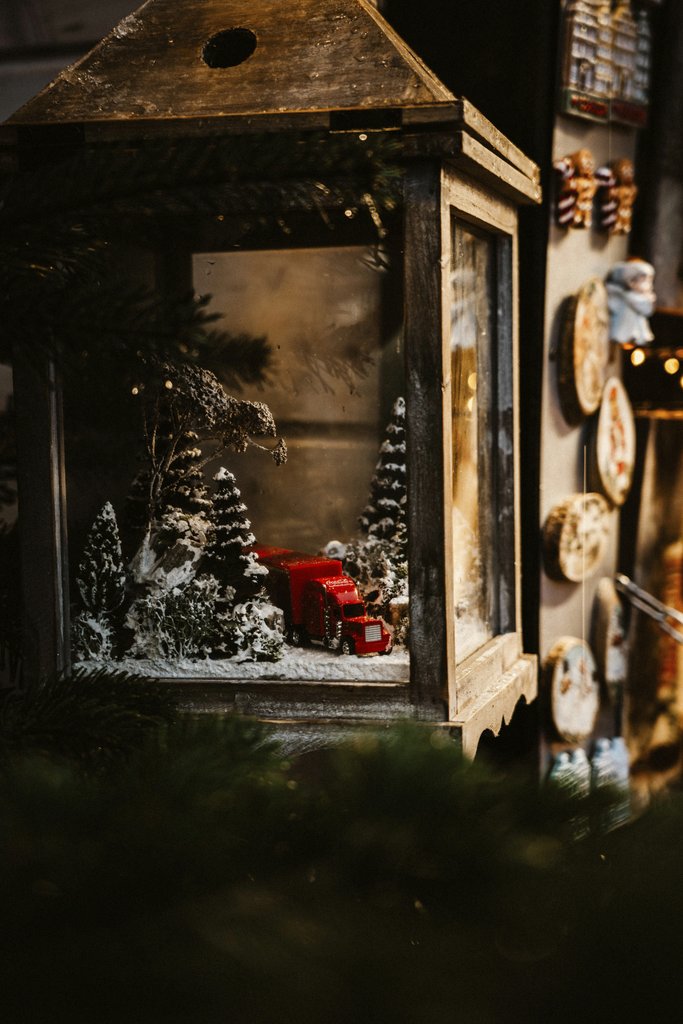 Katia Miasoed - A charming Christmas lantern featuring a miniature red truck and snow-covered trees, creating a warm holiday ambiance.