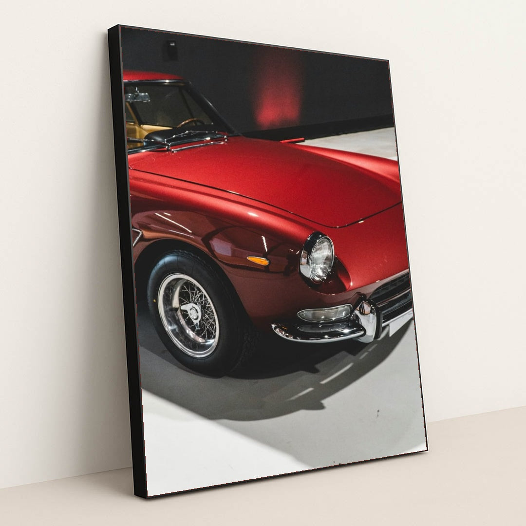 This photo shows a classic Ferrari painted in deep red with wire-spoke wheels, parked indoors under soft lighting, in a black frame.