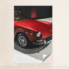 This photo shows a classic Ferrari painted in deep red with wire-spoke wheels, parked indoors under soft lighting, minimalist unframed style.