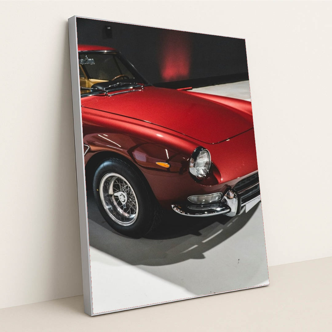 This photo shows a classic Ferrari painted in deep red with wire-spoke wheels, parked indoors under soft lighting, in a silver frame.