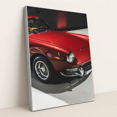 This photo shows a classic Ferrari painted in deep red with wire-spoke wheels, parked indoors under soft lighting, in a silver frame.