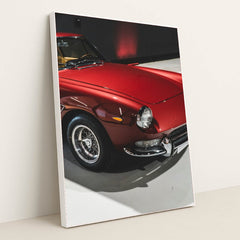 This photo shows a classic Ferrari painted in deep red with wire-spoke wheels, parked indoors under soft lighting, in a white frame.