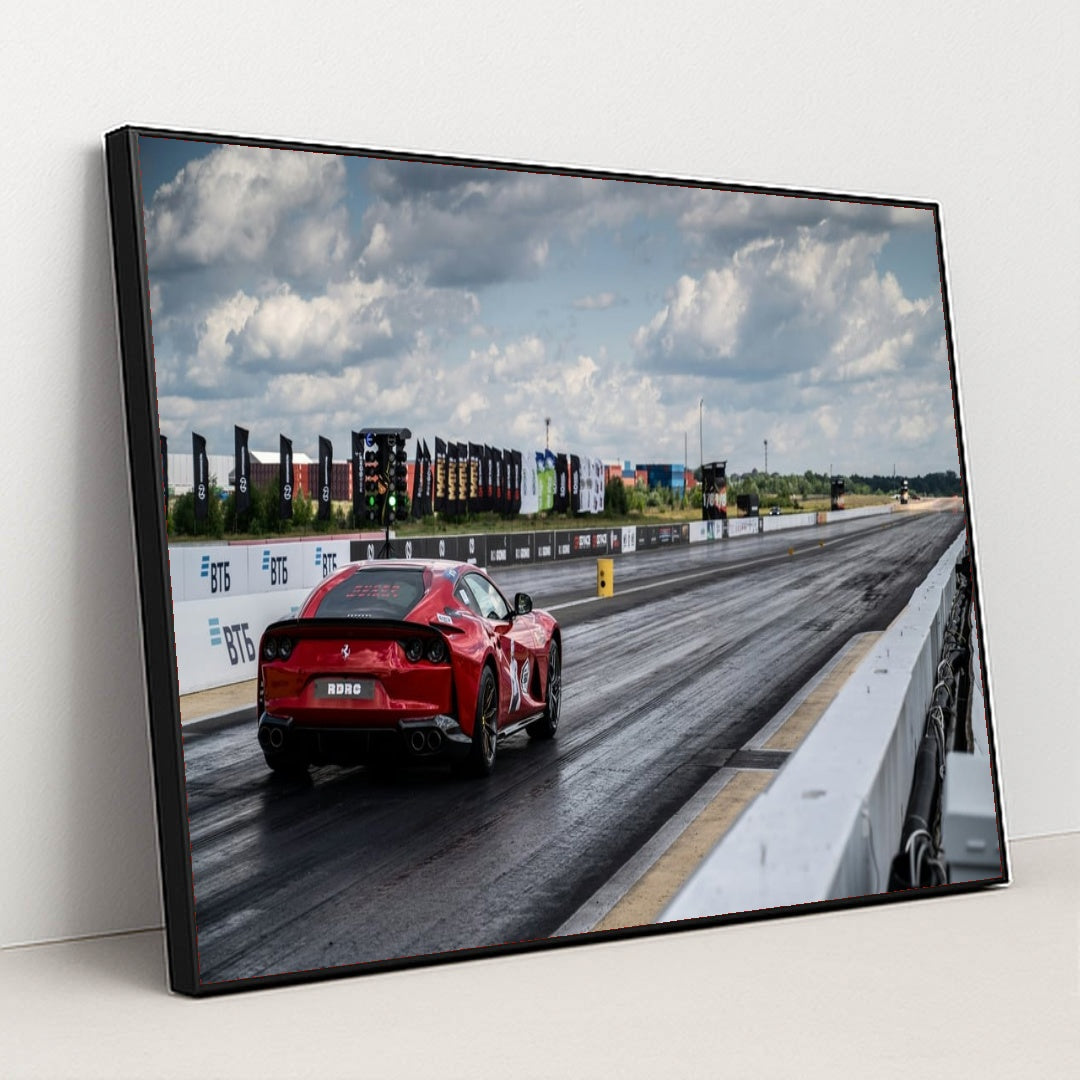 This photo shows a red Ferrari sports car on a dragstrip under a cloudy sky, ready to accelerate, in a black frame.