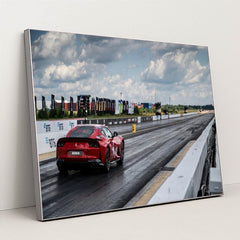 This photo shows a red Ferrari sports car on a dragstrip under a cloudy sky, ready to accelerate, in a silver frame.