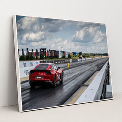 This photo shows a red Ferrari sports car on a dragstrip under a cloudy sky, ready to accelerate, in a white frame.
