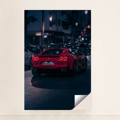 This photo shows a red Ferrari sports car driving at night through city traffic under streetlights, minimalist unframed style.