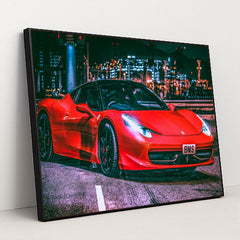 This photo shows a red Ferrari 458 Italia with black wheels parked under city lights at night, in a black frame.