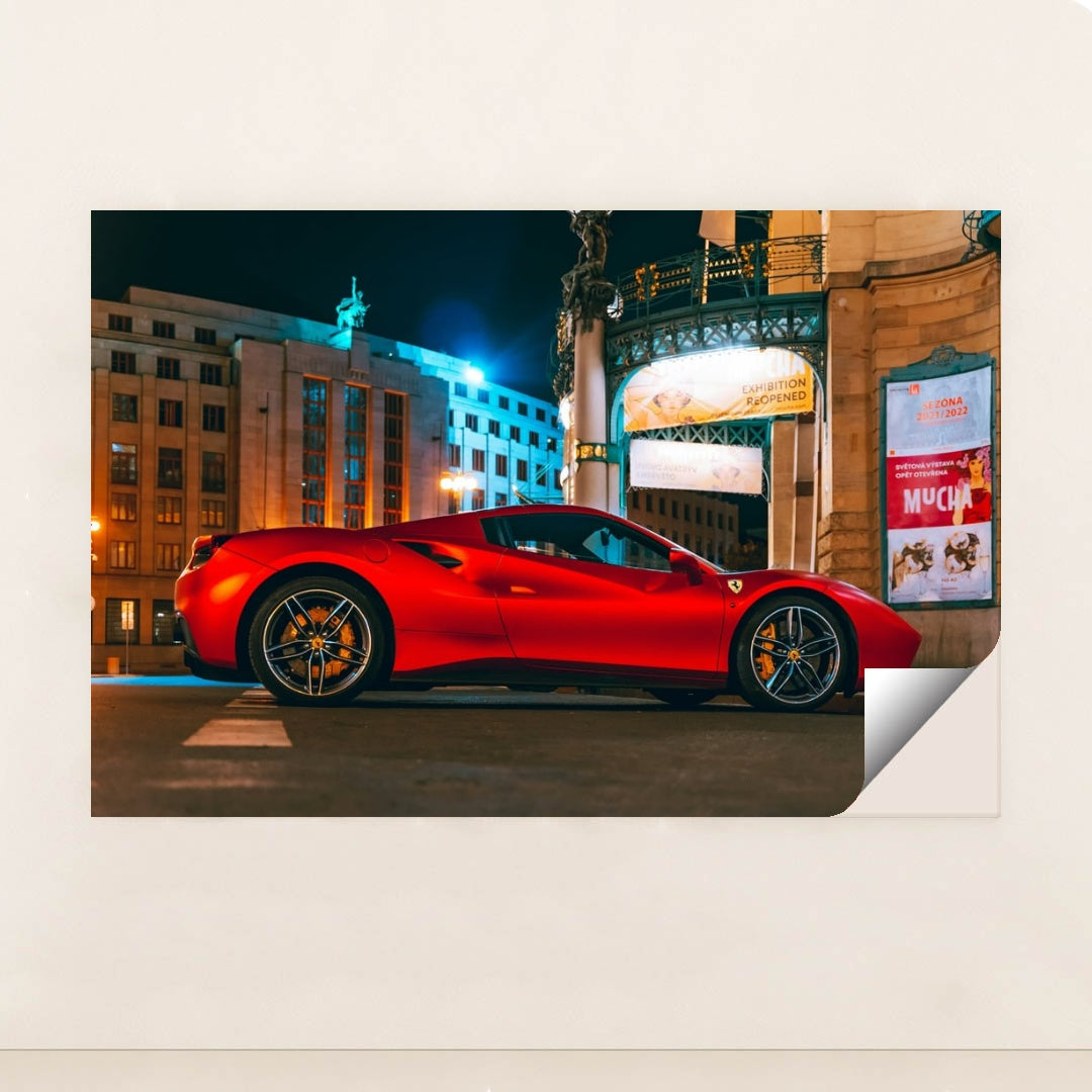 This photo shows a red Ferrari sports car parked in front of an ornate city building at night, under bright streetlights, minimalist unframed style.