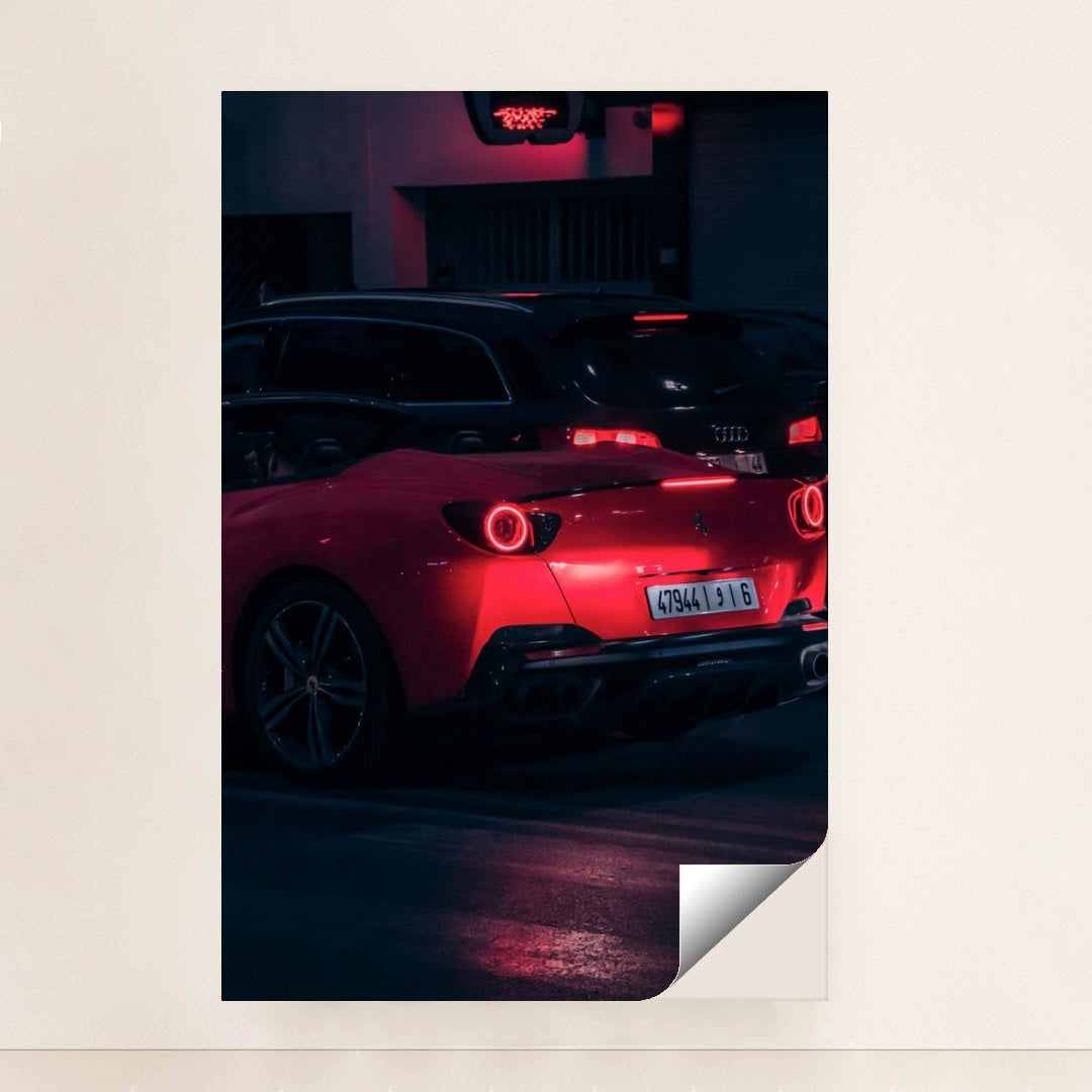 This photo shows a red Ferrari sports car driving at night, illuminated by neon lights, with a black Audi in the background, minimalist unframed style.