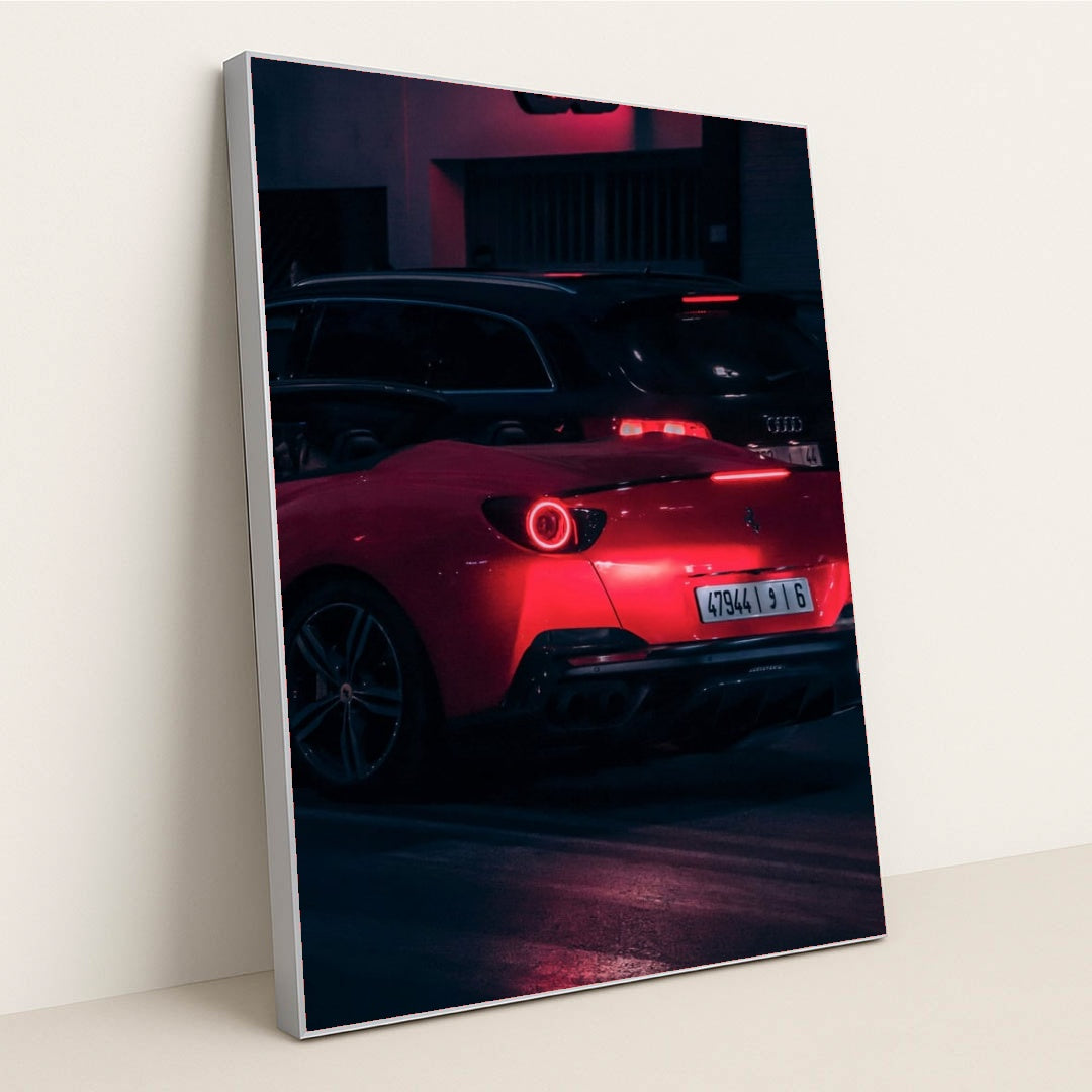 This photo shows a red Ferrari sports car driving at night, illuminated by neon lights, with a black Audi in the background, in a silver frame.